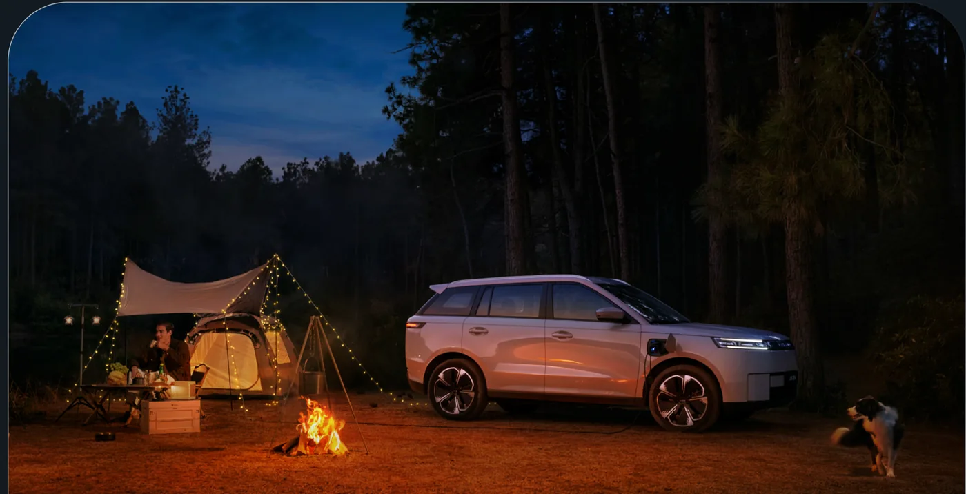 J5 EV parked beside a lit tent and campfire at night.
