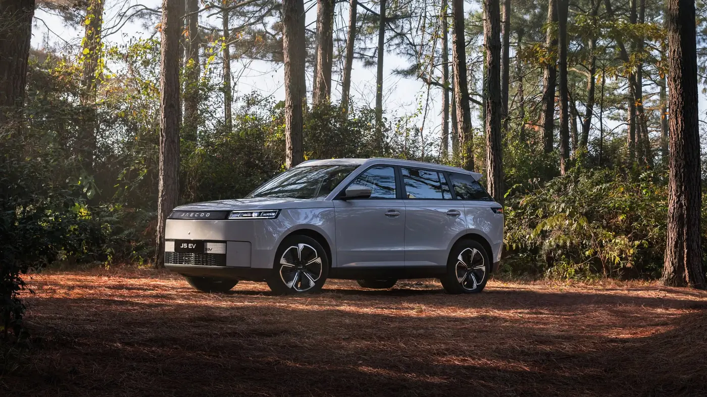 Jaecoo J5 EV parked on a pine forest trail in autumn.
